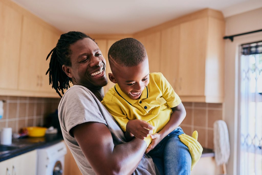 An affectionate young single father playing with his son while cleaning in their kitchen at home