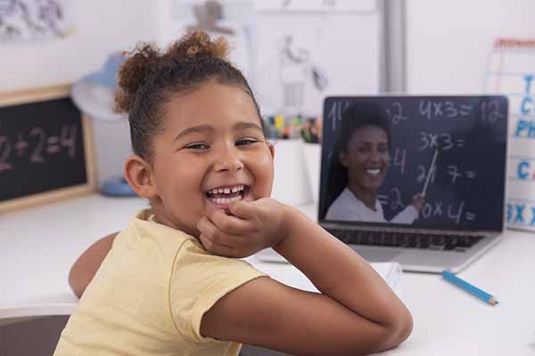 6 years old girl learning at home online, using a laptop computer with a video chat app.