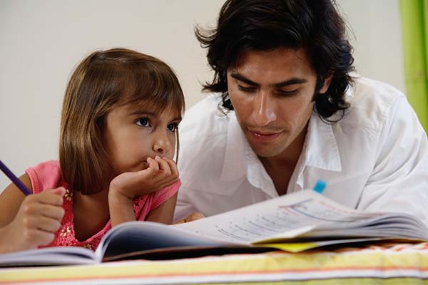 Father helping daughter (8-10) with home-work on bed