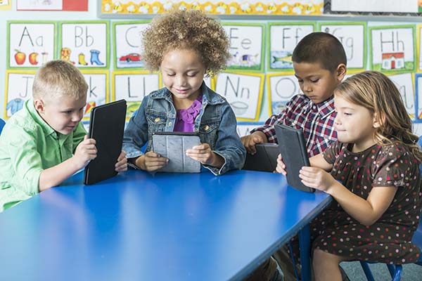 Four children in kindergarten using digital tablets